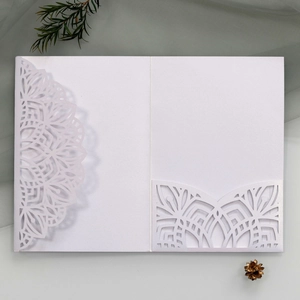 Detailed laser-cut mandala white wedding invitation cover on elegant green gauze background