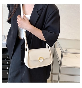 Gros plan sur le sac selle crème avec boucle dorée porté par un mannequin chic