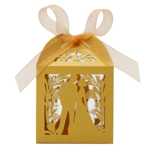 Detail of laser-cut golden favor box featuring a romantic couple silhouette and ribbon