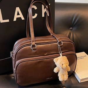 Deep brown leather boston bag with bear charm on a bench in a minimalist city setting