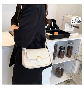 Sac selle chic crème avec boucle dorée porté par un mannequin dans un café élégant