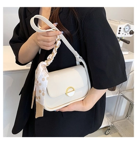 Détail du sac selle crème avec fermoir doré et ruban de soie floral sur la chaîne métal