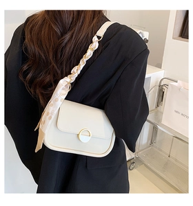 Détail du sac selle blanc cassé avec anneau en métal doré et foulard en soie sur la bandoulière