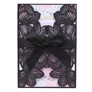 Detail of laser-cut floral wedding invitation with black ribbon and floral inner card