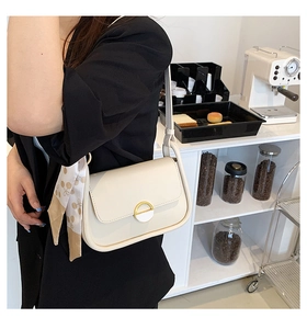 Détail du sac selle crème avec boucle dorée et foulard fleuri dans un café chic
