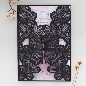 Detail of laser-cut black wedding invitation sleeve with floral insert on white background