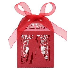 Detail of red laser-cut wedding favor box featuring bride and groom silhouette with ribbon