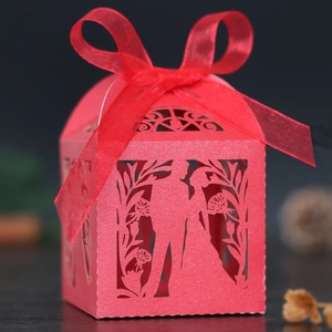 Macro shot of laser-cut red wedding favor box with ribbon bow and couple silhouette