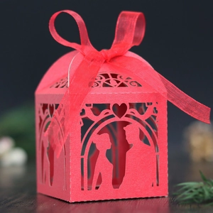 Close-up of laser-cut wedding candy box featuring a romantic couple and red silk ribbon