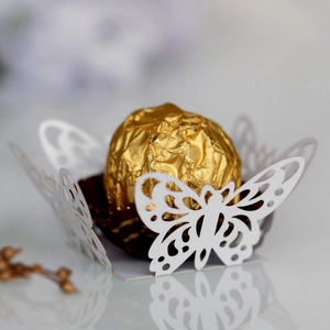 Macro view of white laser-cut butterfly candy box with a golden chocolate ball