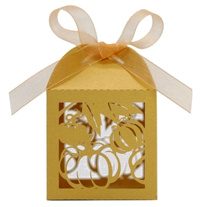 Macro detail of laser-cut pumpkin pattern on a golden paper favor box with silk ribbon