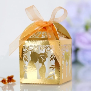 Detail of golden laser-cut wedding candy box featuring kissing couple silhouette and ribbon