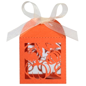 Detail of laser-cut orange pumpkin favor box with elegant white ribbon bow for parties