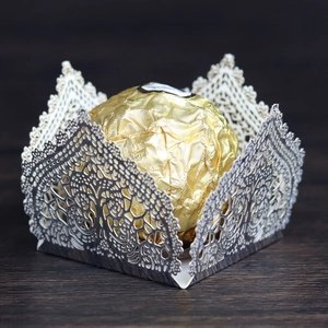 Detail view of silver laser-cut lace cupcake liner with floral patterns on wood surface