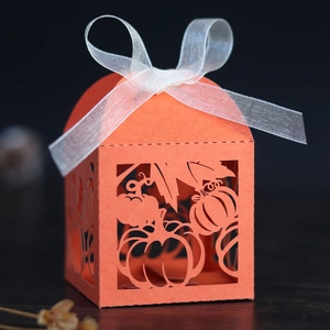 Detail of orange laser-cut pumpkin favor box with maple leaf design and white ribbon bow