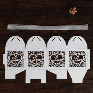 Macro detail of laser-cut LOVE paper favor box with intricate vine pattern and ribbon