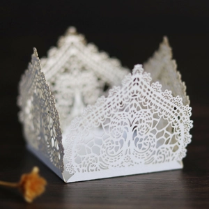 Detail of white laser-cut favor box featuring elegant lace patterns on dark wood