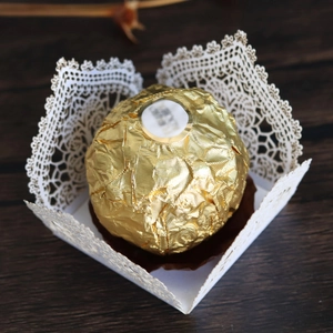 Detailed laser-cut lace chocolate wrapper with elegant white pattern on wood background