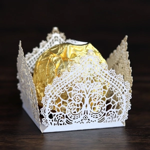 Detailed laser-cut white lace paper candy holder with golden chocolate on wood