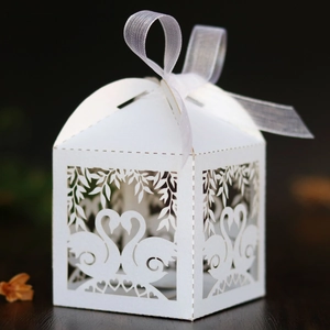 Close-up of laser-cut white wedding favor box with swan heart design and ribbon