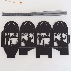 Flat lay of laser-cut black paper party favor box with western cowboy and cactus silhouettes