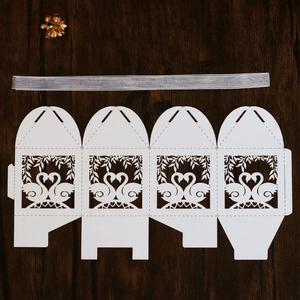 Flat lay of white laser-cut wedding favor box with swan heart design and satin ribbon