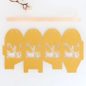 Flat lay of gold laser-cut pumpkin favor box template with pink ribbon for Thanksgiving