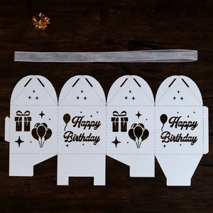 Flat lay of laser-cut Happy Birthday paper gift box with white balloons and silver ribbon