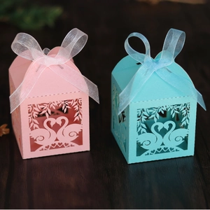 Detail of laser-cut heart swan candy boxes with organza ribbons in pink and blue colors