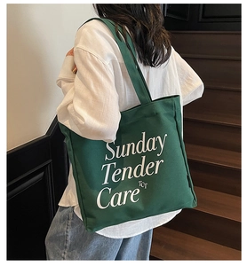 Dettaglio della borsa tote in tela verde scuro con scritte bianche su sfondo legno