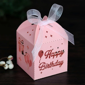 Detailed view of pink laser-cut Happy Birthday candy box with white ribbon on dark wood
