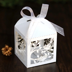 Detail of laser-cut wedding favor box with bird and flower hollow pattern and white ribbon
