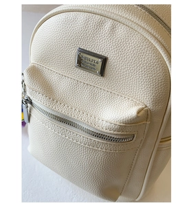 Gros plan sur la texture grainée beige et le logo métallique argenté du sac à dos