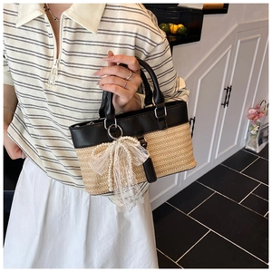 Detail of hand-woven straw tote bag with black leather trim and lace pearl bow ornament