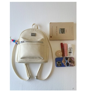 Vue à plat d'un mini sac à dos crème avec texture cuir litchi et détails en métal argenté