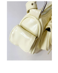 Détail d'un sac à bandoulière beige brillant avec poche latérale à rabat et boucles en métal