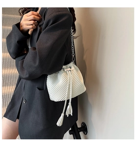 On-body shot of white quilted bucket bag with silver chain strap and tassel drawstring