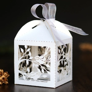 Detail of laser-cut bird pattern on white paper wedding favor box with a satin ribbon bow