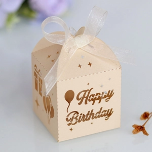 Detailed laser-cut Happy Birthday candy box in champagne paper with a white ribbon bow