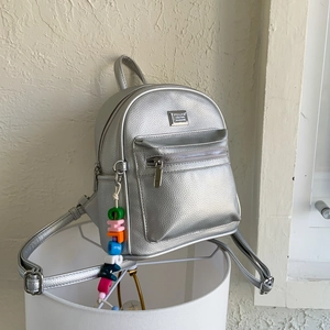 Détail d'un mini sac à dos en cuir argenté grainé avec breloque lettre Cherish colorée