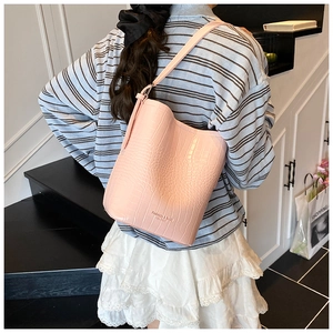 Detail of pink croc-embossed leather bucket bag worn by model with textured strap finish