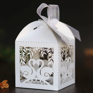 Detail of laser-cut white wedding favor box with swan heart pattern and silk ribbon