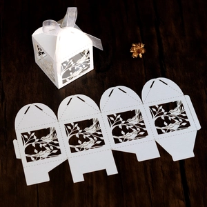 Detail of laser-cut wedding favor box with bird patterns and white ribbon on wood surface