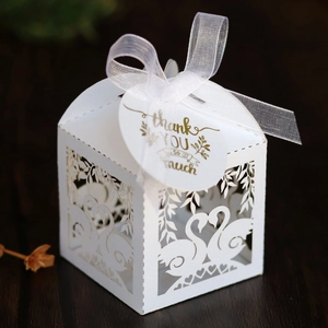 Detail of white laser-cut swan candy box with elegant ribbon and thank you tag