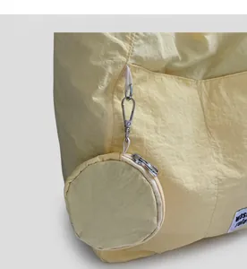 Detail of pale yellow nylon tote bag with hanging round coin purse and logo patch