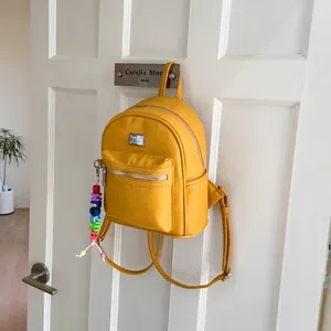 Détail d'un mini sac à dos en cuir PU jaune vif avec zips argentés sur un crochet de porte