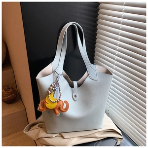 Detail of light blue lychee pattern tote bag with leather elephant charm in soft sunlight