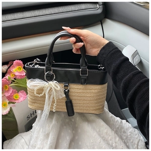 Detail of woven straw handbag featuring black leather trim and pearl bow charm