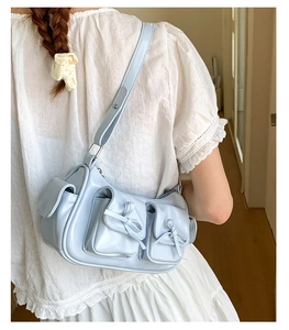 Détail du sac bandoulière bleu clair avec nœuds décoratifs et multiples poches utiles