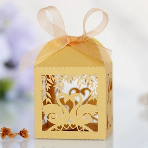 Detail of laser-cut gold wedding favor box featuring swan heart motifs and organza ribbon